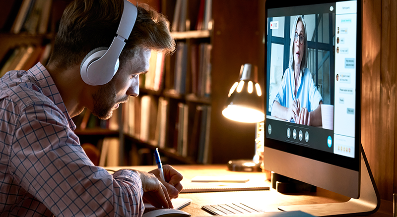 Man in headphones taking notes from online meeting